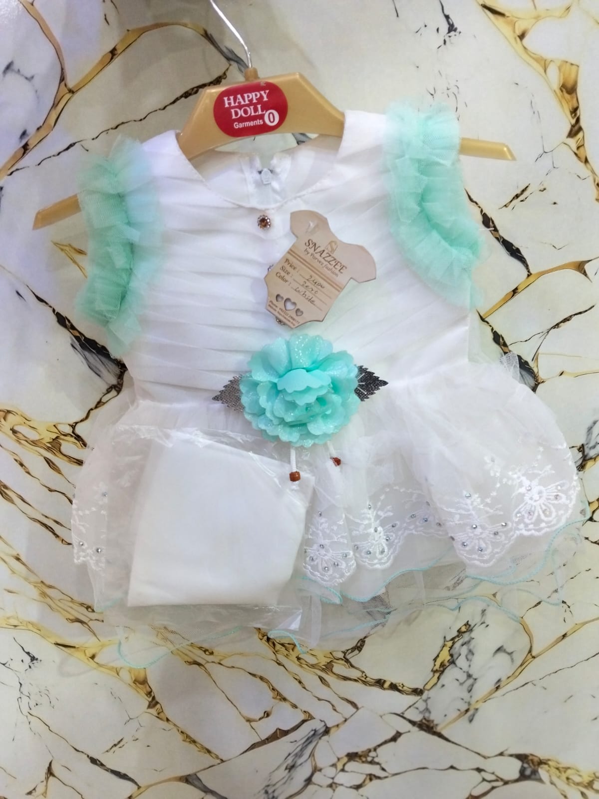 White baby dress with green ruffles and flowers on a marble surface